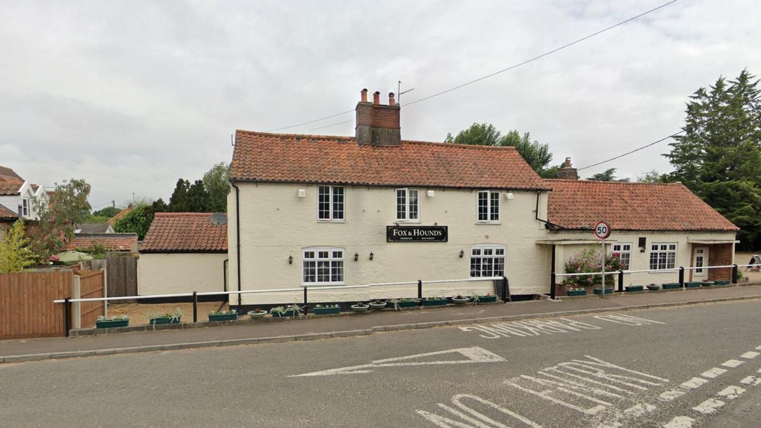 Roadside view of Fox and Hounds pub, a cream double-storey building with a single-storey extension. It is located on the side of a road. 