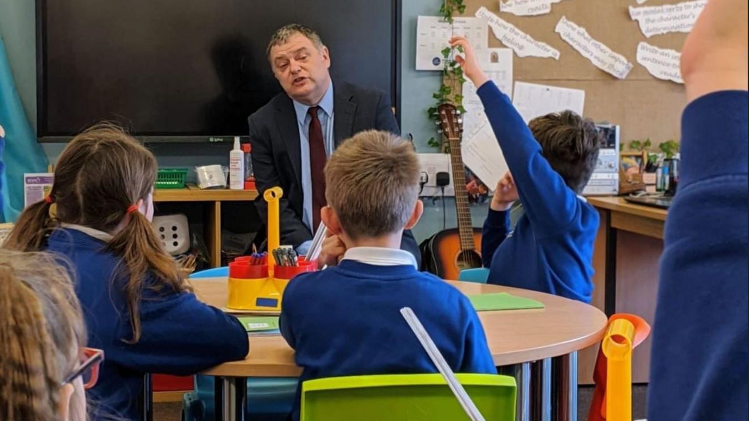 MP Mike Amesbury sat in a classroom with school children wearing blue jumpers