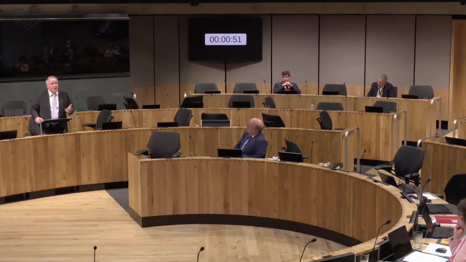 Senedd Cymru A shot of the Senedd chamber showing a large number of empty chairs, with a few members still present.