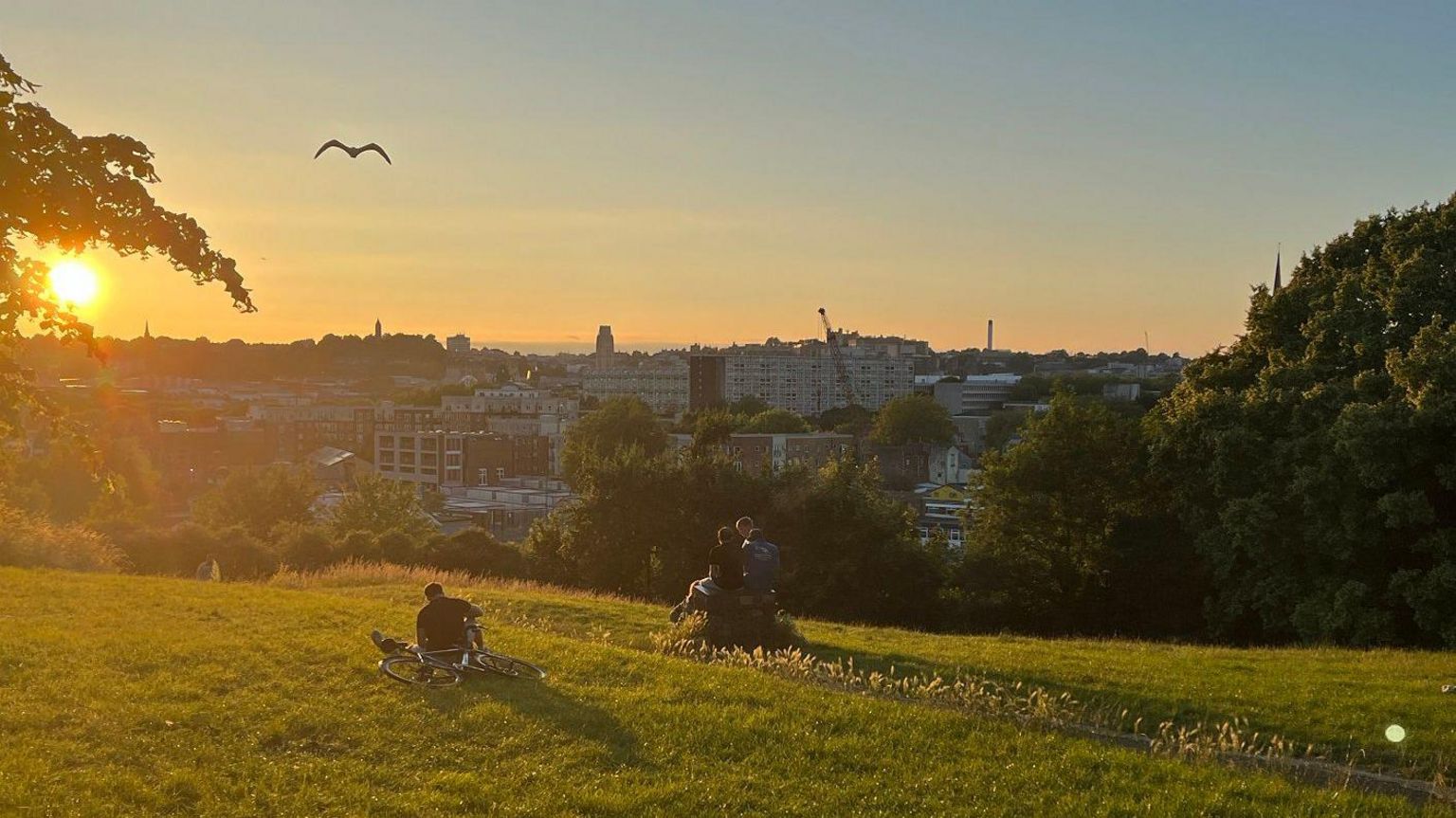People watch the sun set from Victoria Park in Bristol. Bristol city centre is visible in the background.