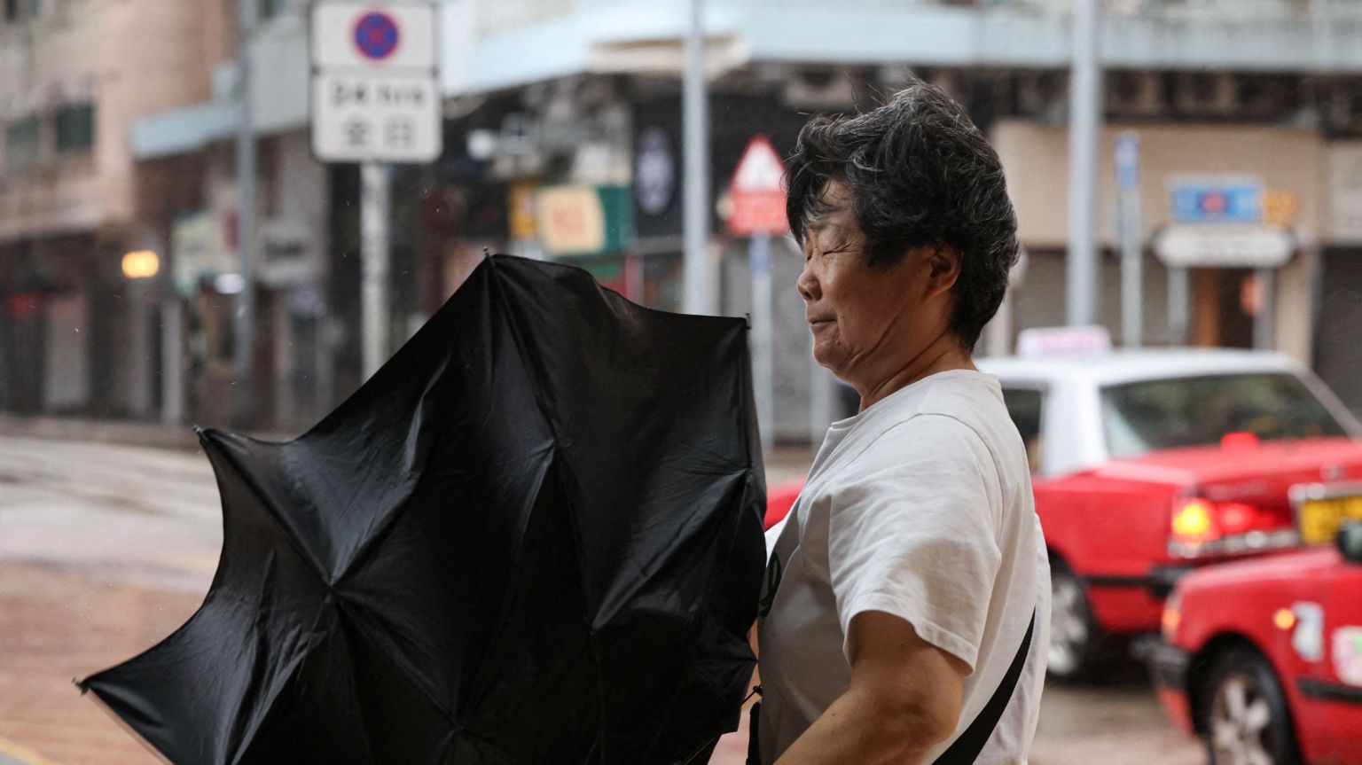 一名行人在香港受台风“罗莎”（Noul）带来的暴雨和强风影响下撑伞前行；强风吹得雨伞向上翻起