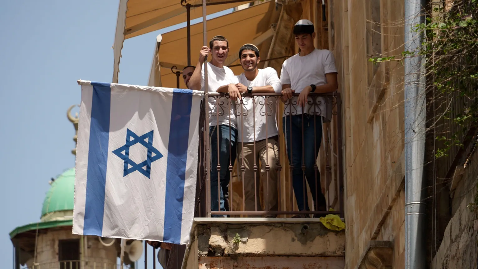 A group of Israeli settlers stand in a balcony with an Israeli flag in Jerusalem's Old City.