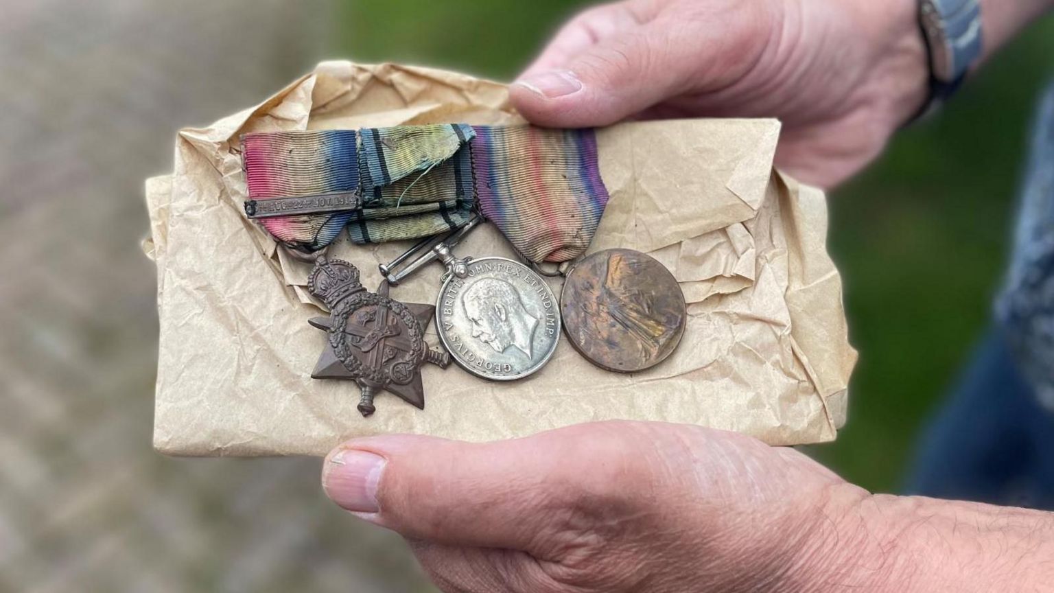 Three old medals in tissue paper are held in a man's hands.