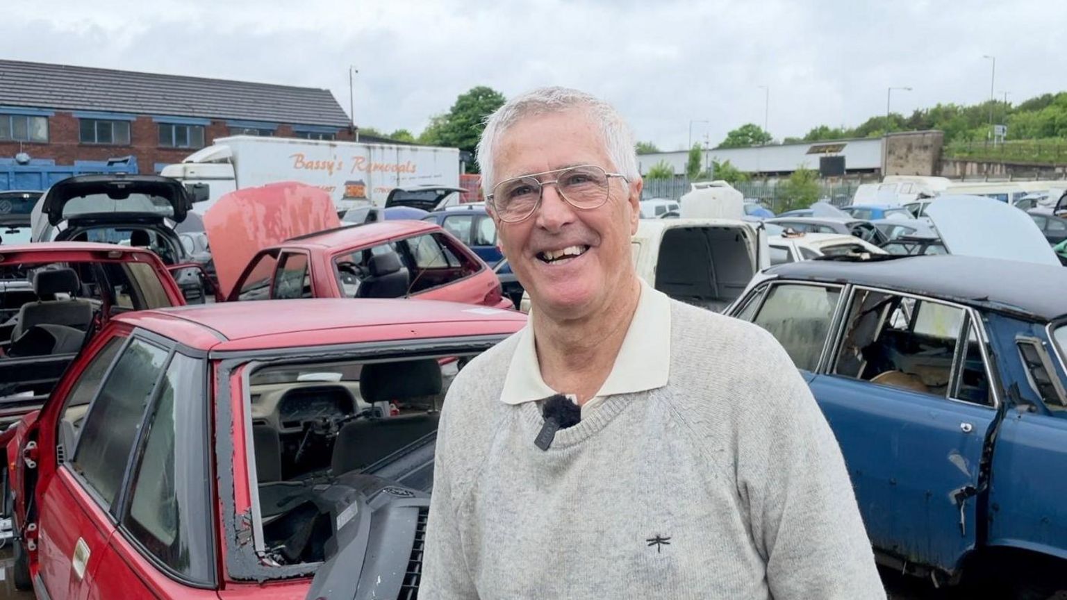 Lawrence Curley stands in front of scrap cars