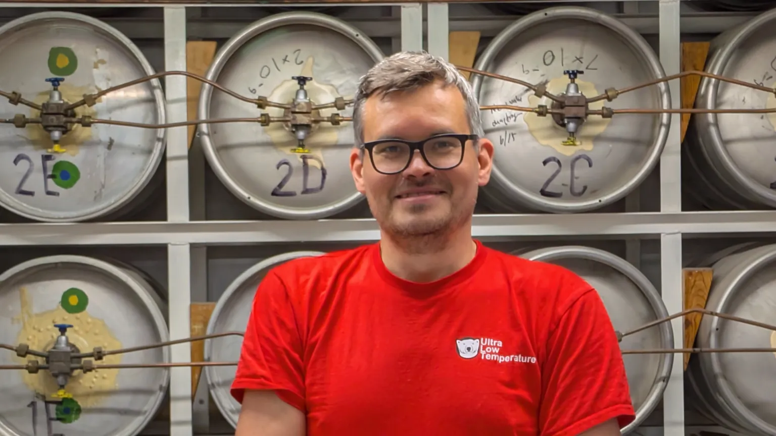 Jacob Clothier/Lancaster University In a red t-shirt Dima Zmeev stands in front of metal kegs containing helium-3.