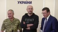 Arkady Babchenko stands between two men at an official press conference event