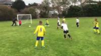 A dad about to push his goalkeeper son to stop the ball going into the net