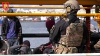 A Maltese soldier stands by migrants onboard Elhiblu 1