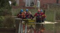 Rescuers guide a woman in a dinghy in flood water