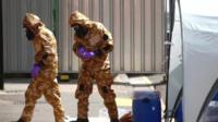 Investigators in hazardous material suits enter building