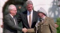 US President Bill Clinton standing between PLO leader Yasser Arafat as he shakes hands with Israeli Prime Minister Yitzhak Rabin