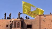 US-backed Syrian Democratic Forces (SDF) raising their flag atop a building in the Islamic State group's last stronghold in the eastern Syrian village of Baghuz, 23 March 2019