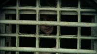 A young man looks through the bars of a prison