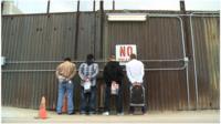 Immigrants about to be deported from US to Mexico line up against the border fence