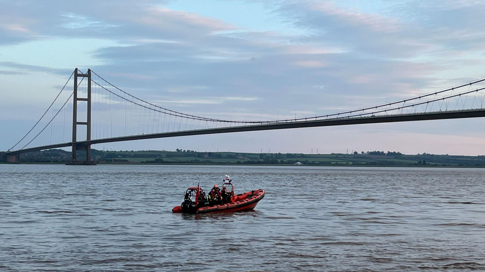 A Humber Rescue boat laying a poppy wreath in the water with Humber Bridge in the background