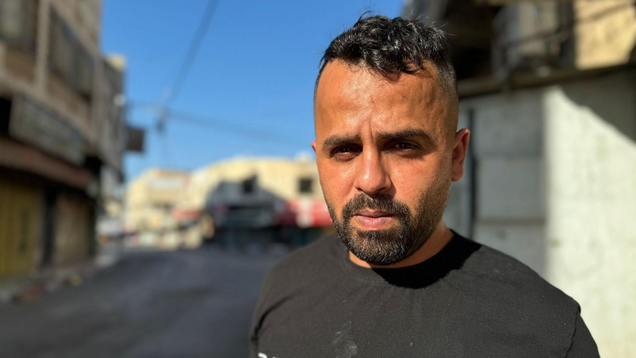 Thaeer Shana’at looking at the camera, with a Jenin street in the background