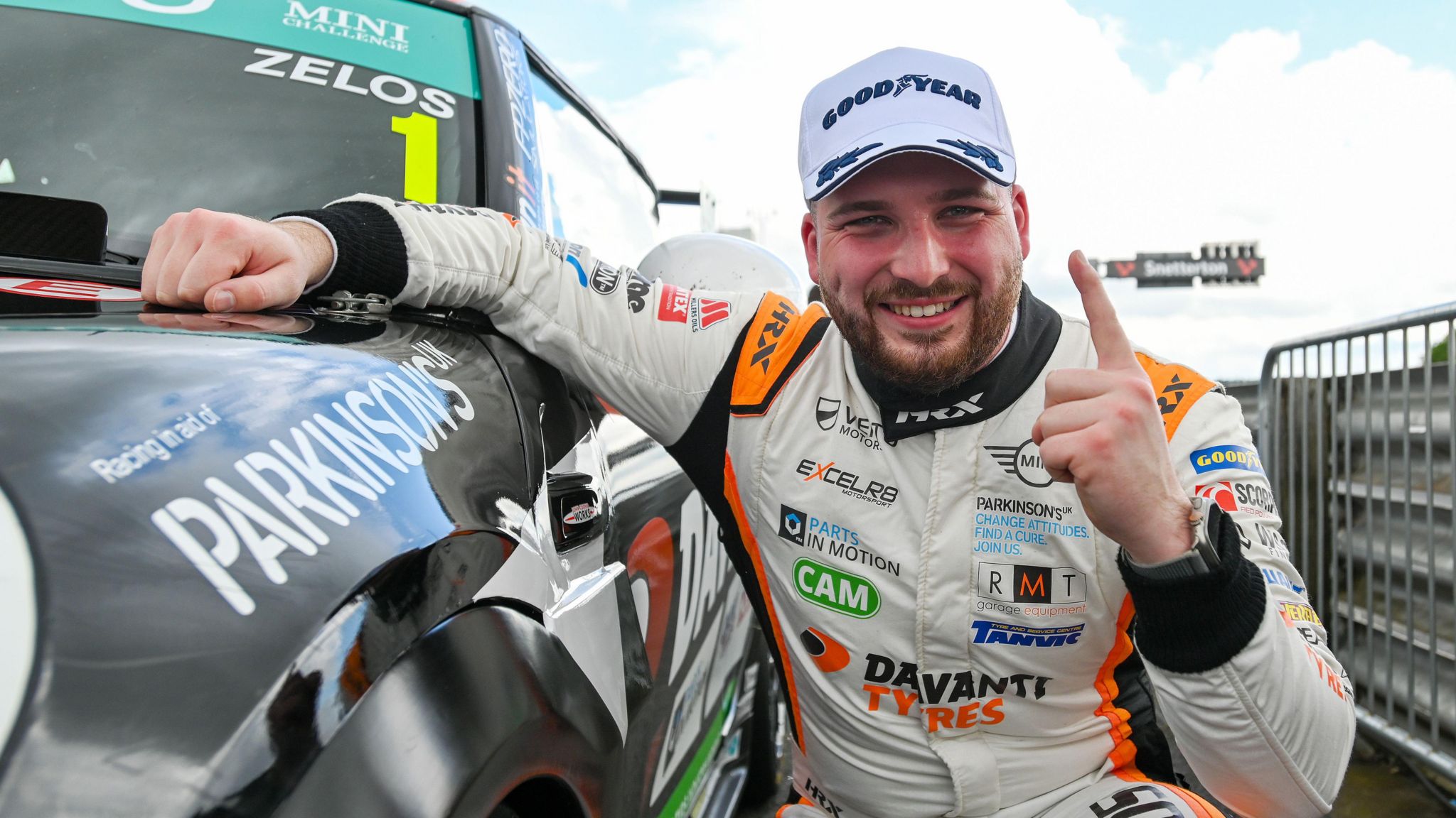 Dan Zelos makes a 'number 1' sign crouched next to his racing car to celebrate a victory.