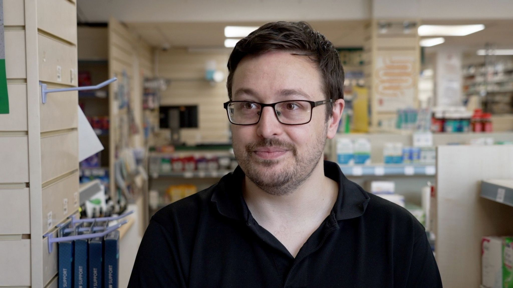 Mark Jackson in a dark shirt and glasses standing in his pharmacy