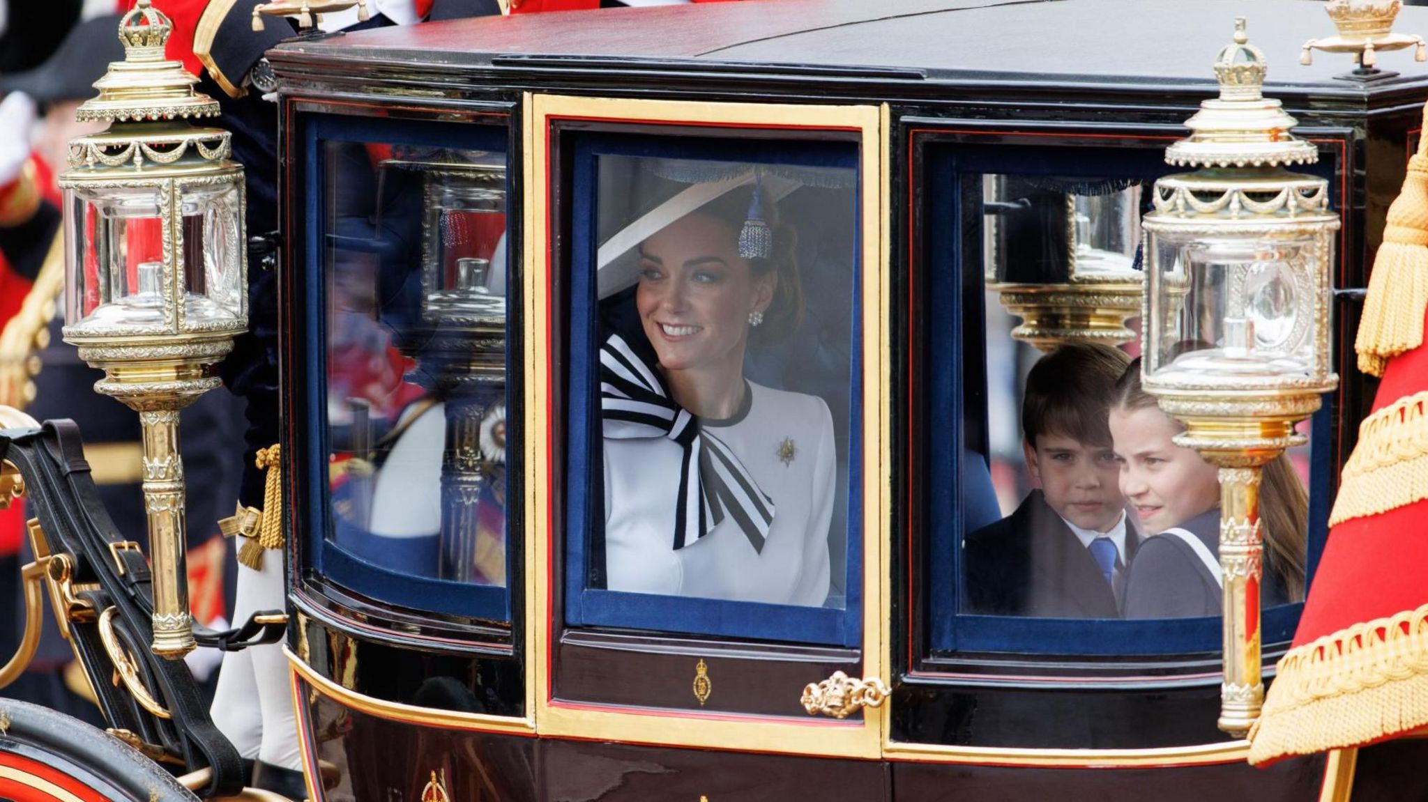 Catherine smiling as she looks through gold carriage window, alongside Louis and Charlotte