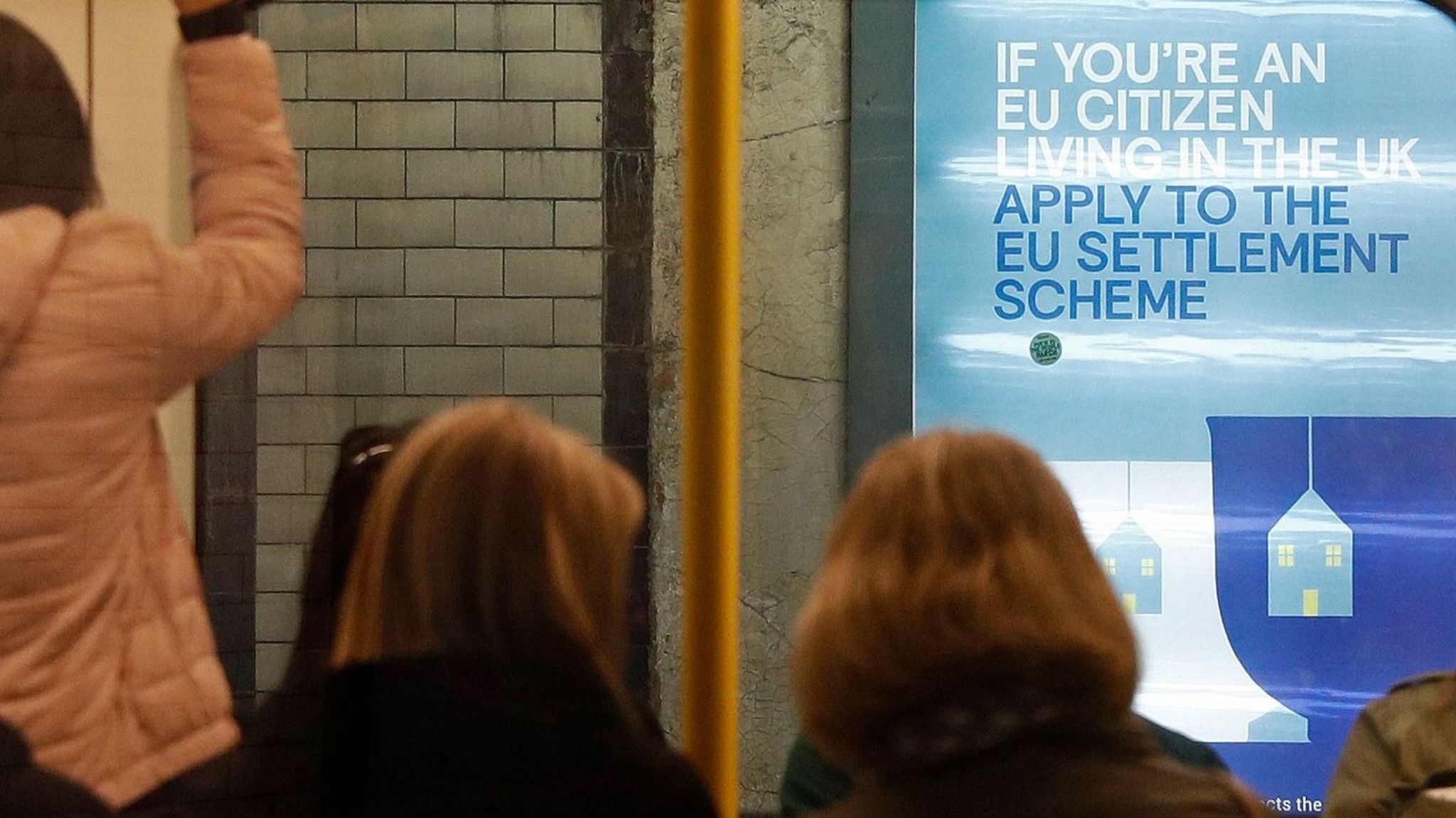 A poster encouraging EU nationals to apply to the government's post-Brexit EU settlement scheme is pictured through a carriage of a London Underground tube train