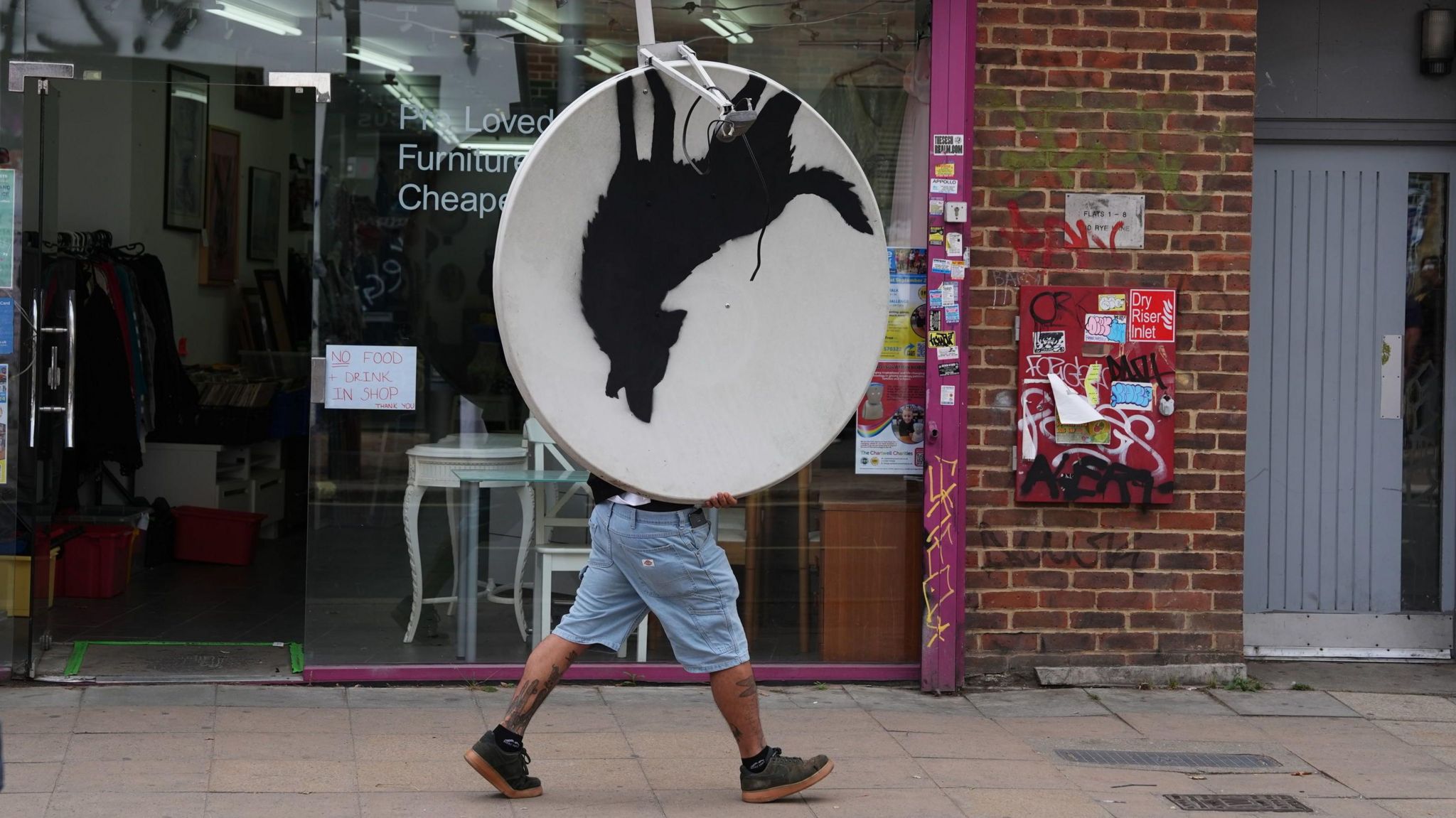 People remove a new artwork by Banksy, depicting a howling wolf painted on a satellite dish that was placed on a shop roof in Peckham, south London