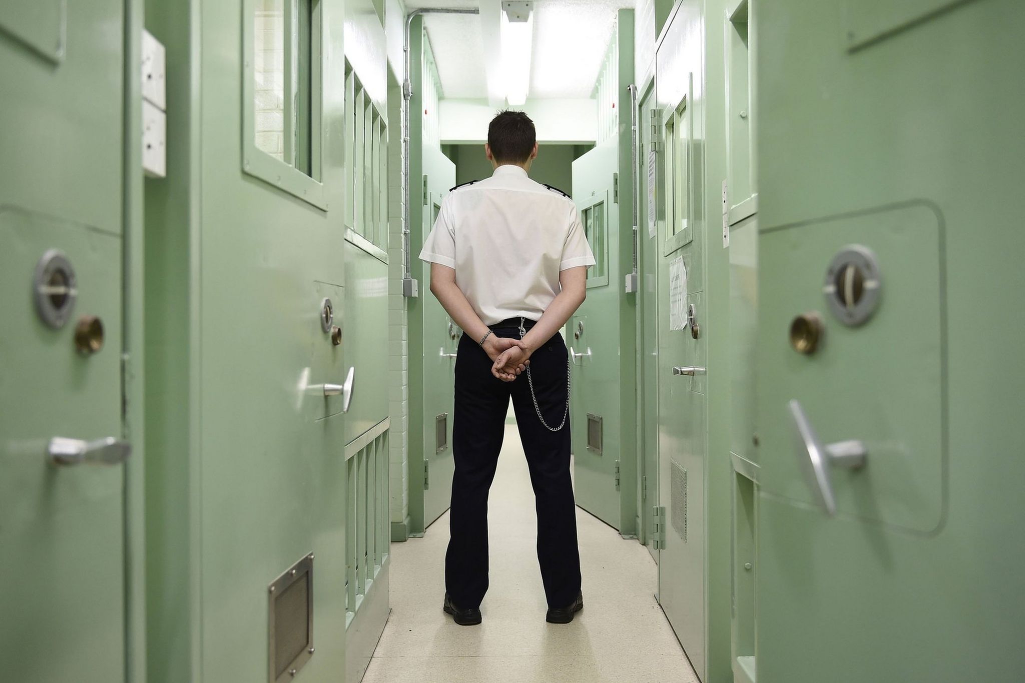 A prison guard stands in the corridor of a prison with his back to the camera.
