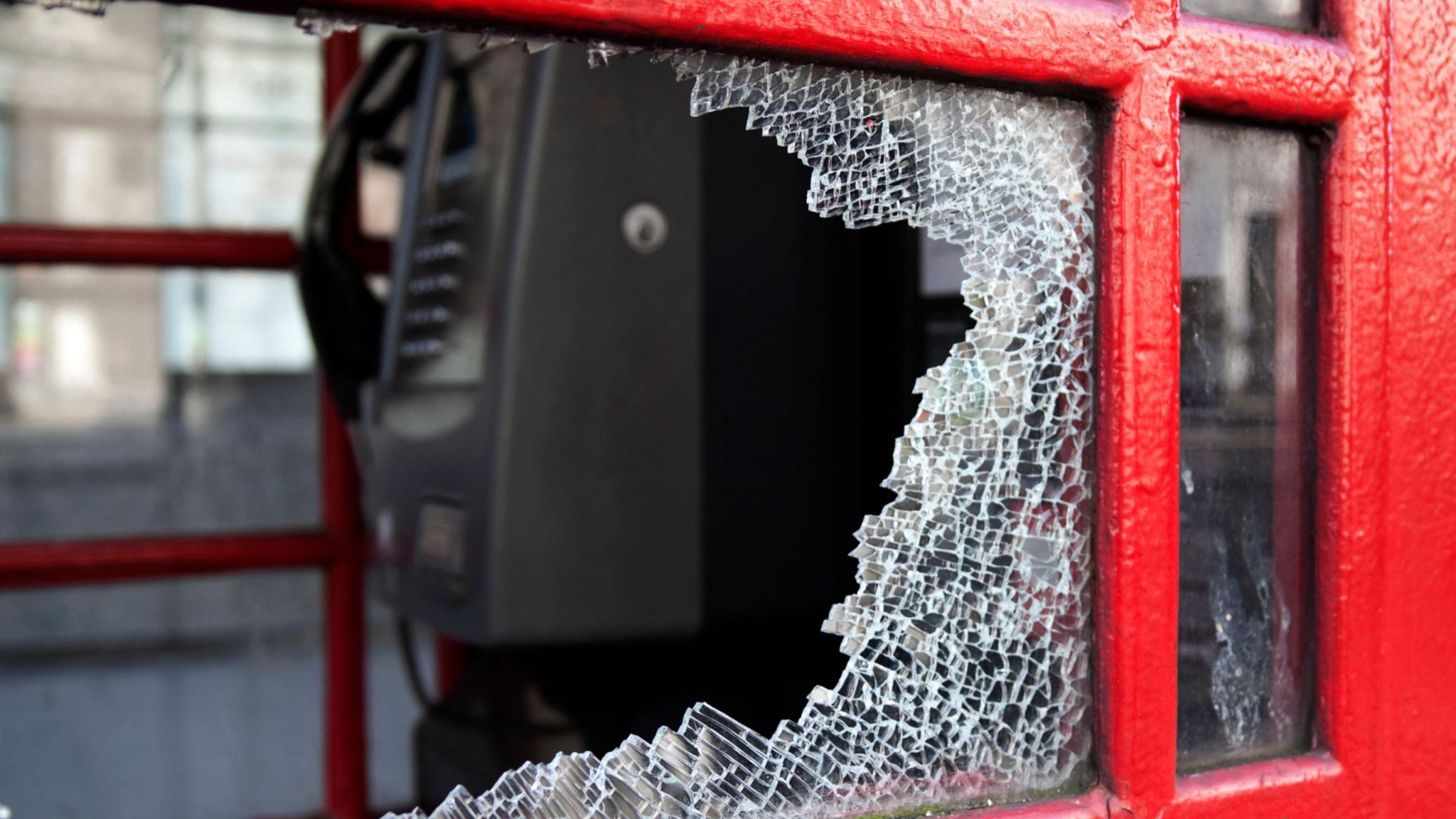 A red phone box with a shattered glass window 