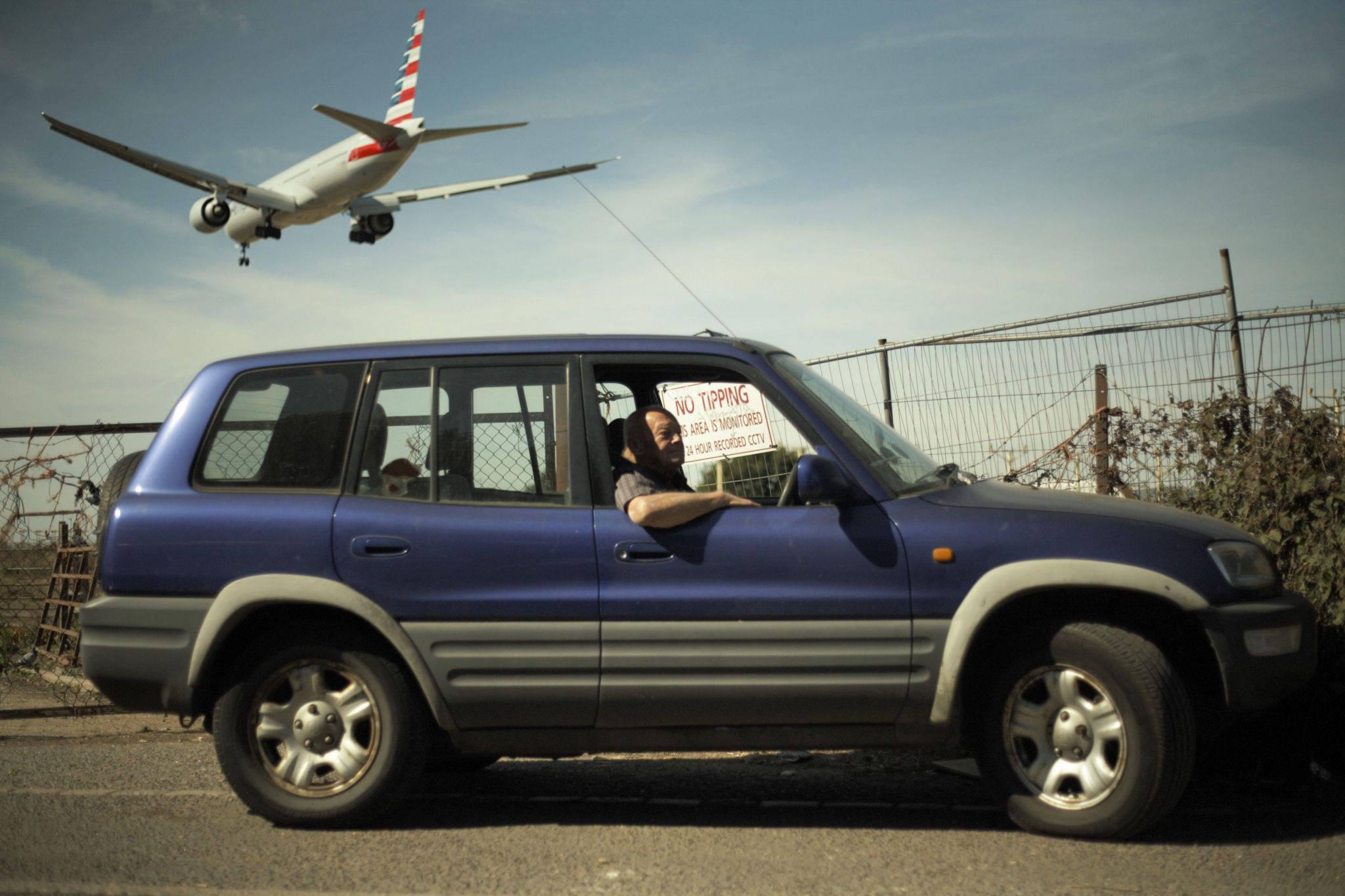 Man in car looks out of the window as a flight passes overhead