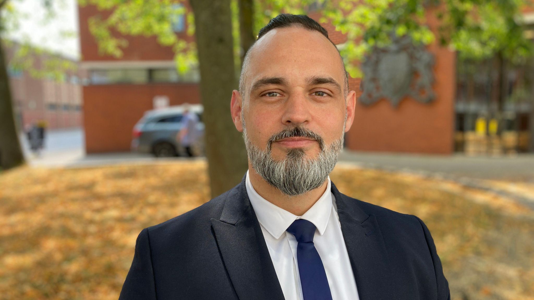 Aaron Rowe wearing a black suit and blue tie standing outside the front of Swindon Crown Court