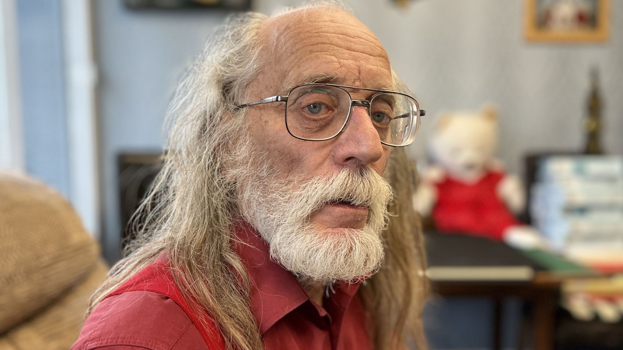 James Leonard with long grey hair and beard wearing glasses and a red shirt