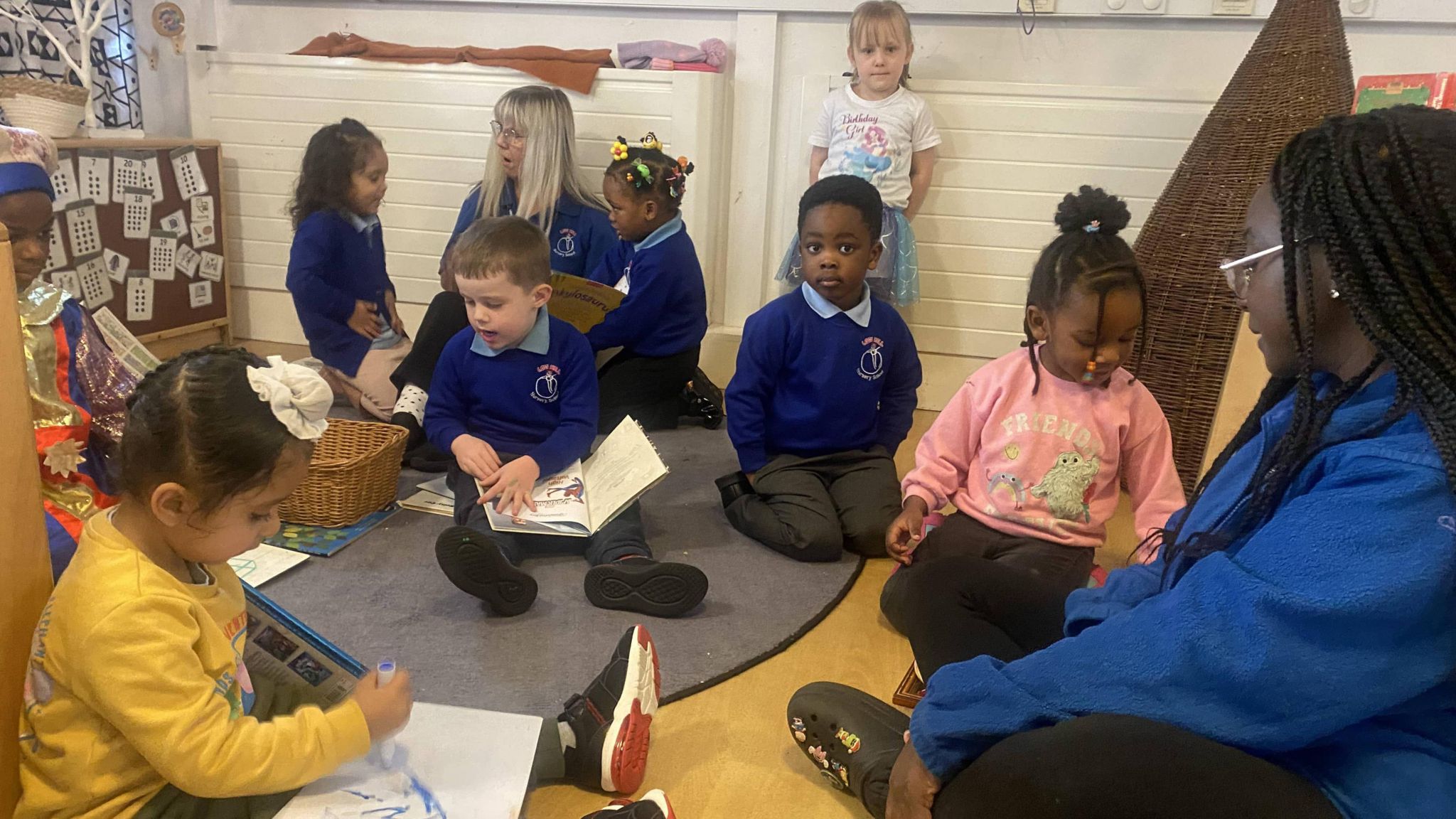 Nursery children reading and playing with teachers 