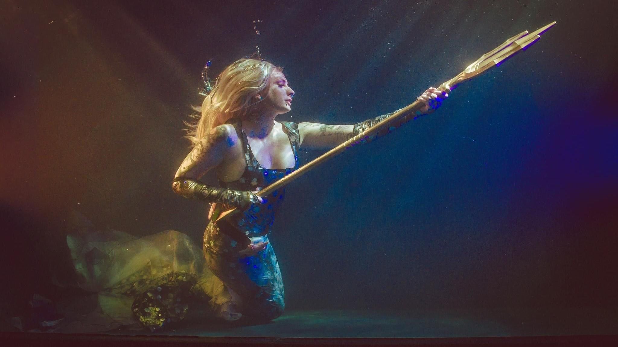 Tyler Turner holding a trident and wearing a mermaid tail and top, and a blonde wig.