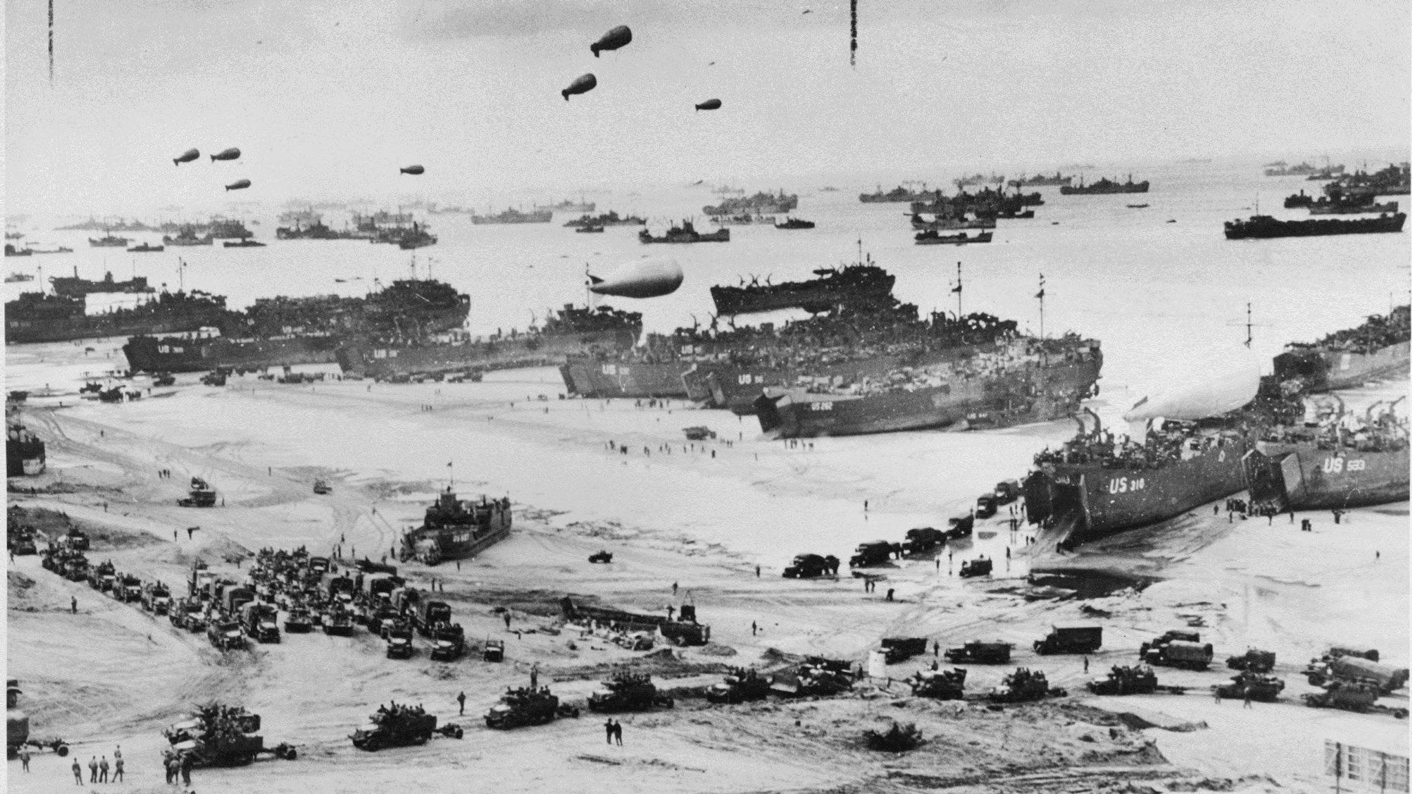 A black and white photo of allied forces landing on Normany beaches, including tanks and ships