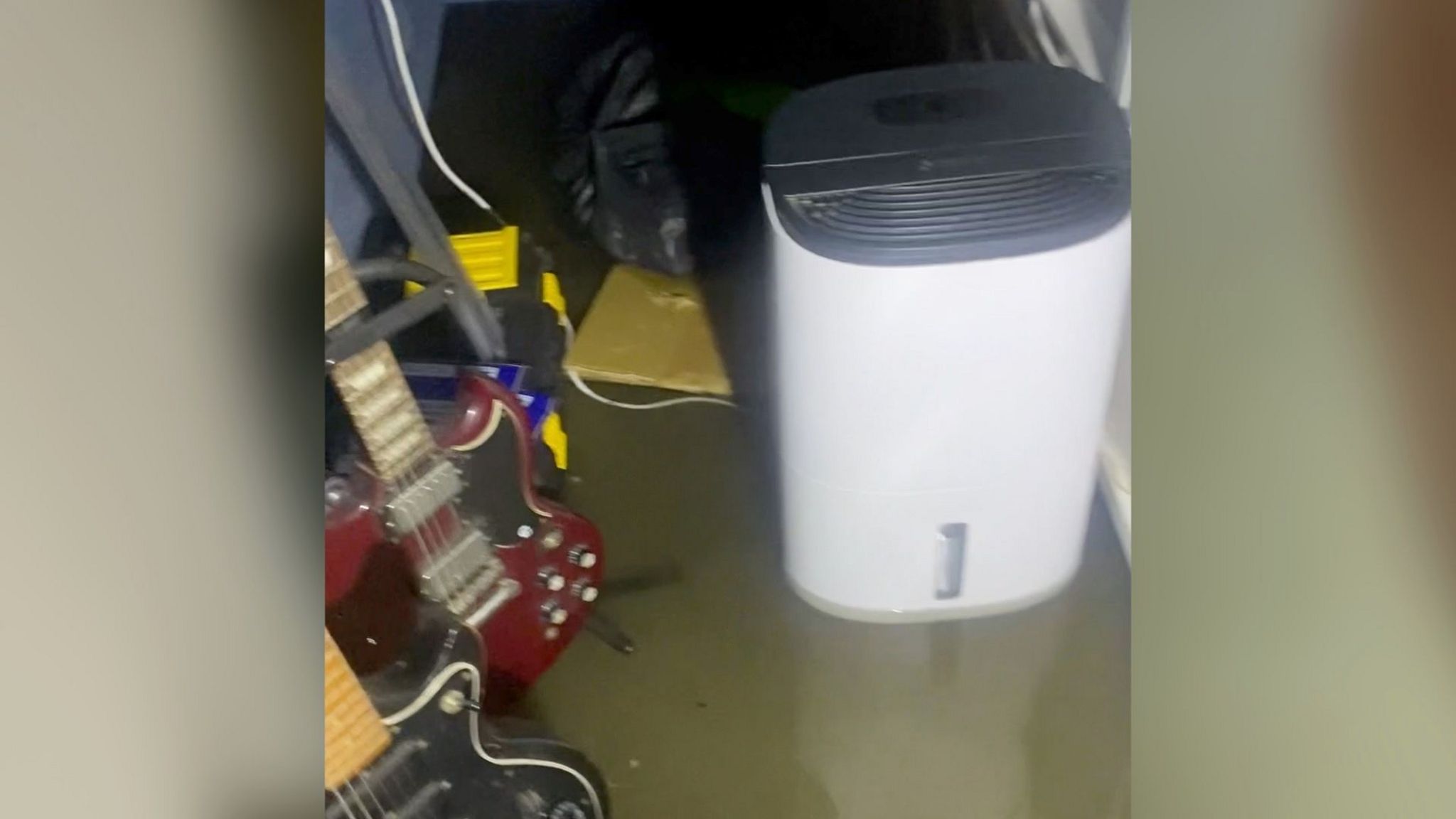 A dehumidifier and electric guitars sitting in water in the basement of the house