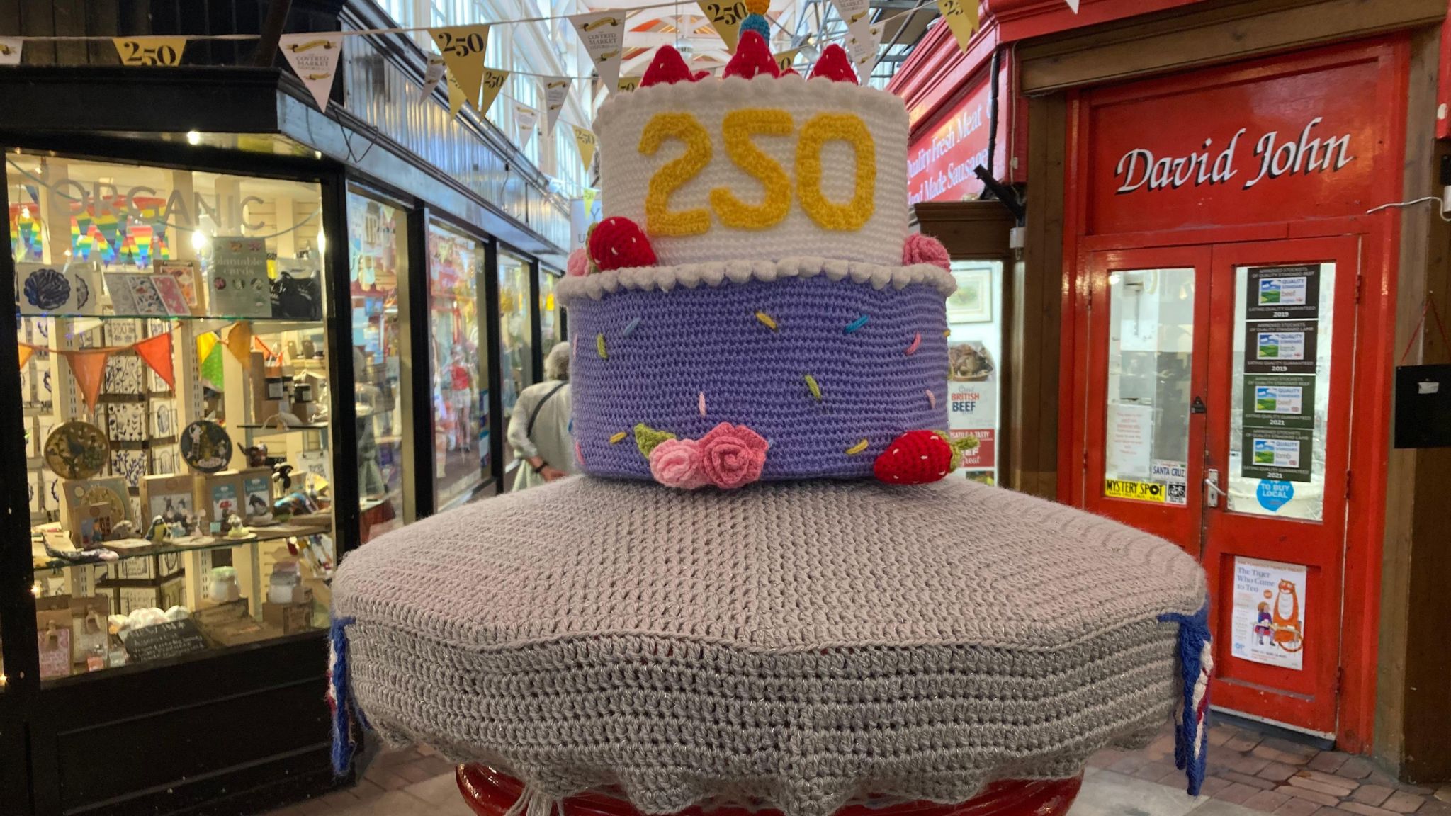 The postbox in the market covered in crocheted yarn in the shape of a 250th birthday cake.