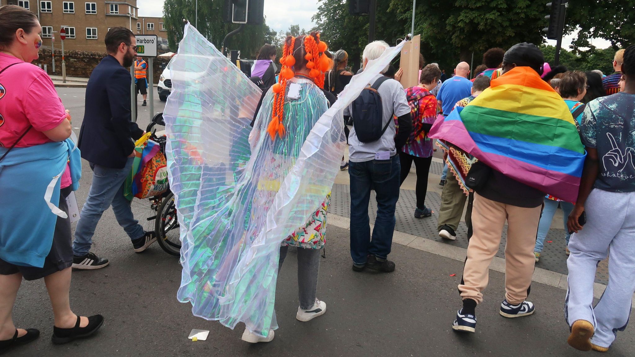 People crossing a busy road with one dressed in a white winged costume