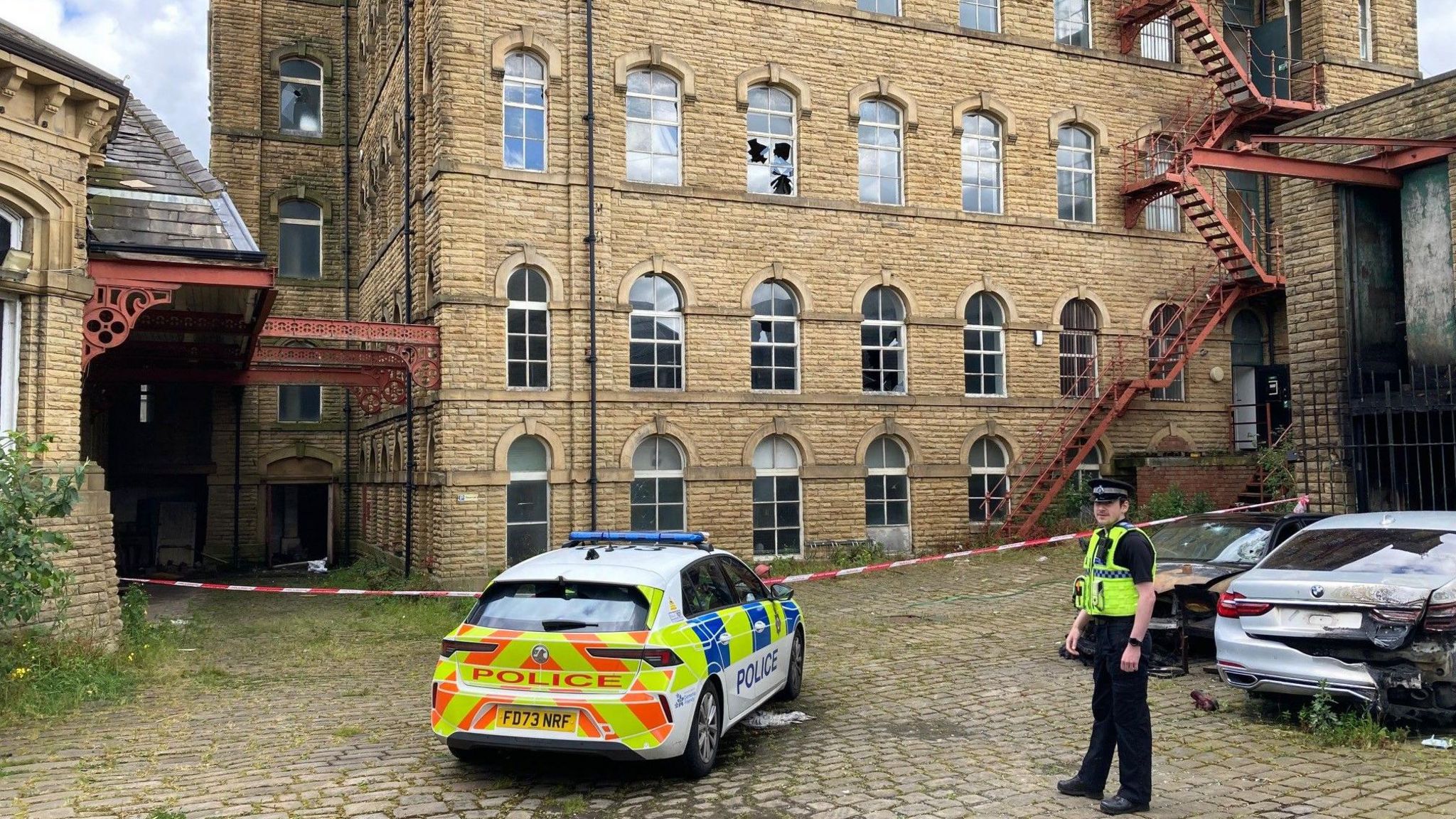A policeman stands next to cordon outside one of the mill buildings