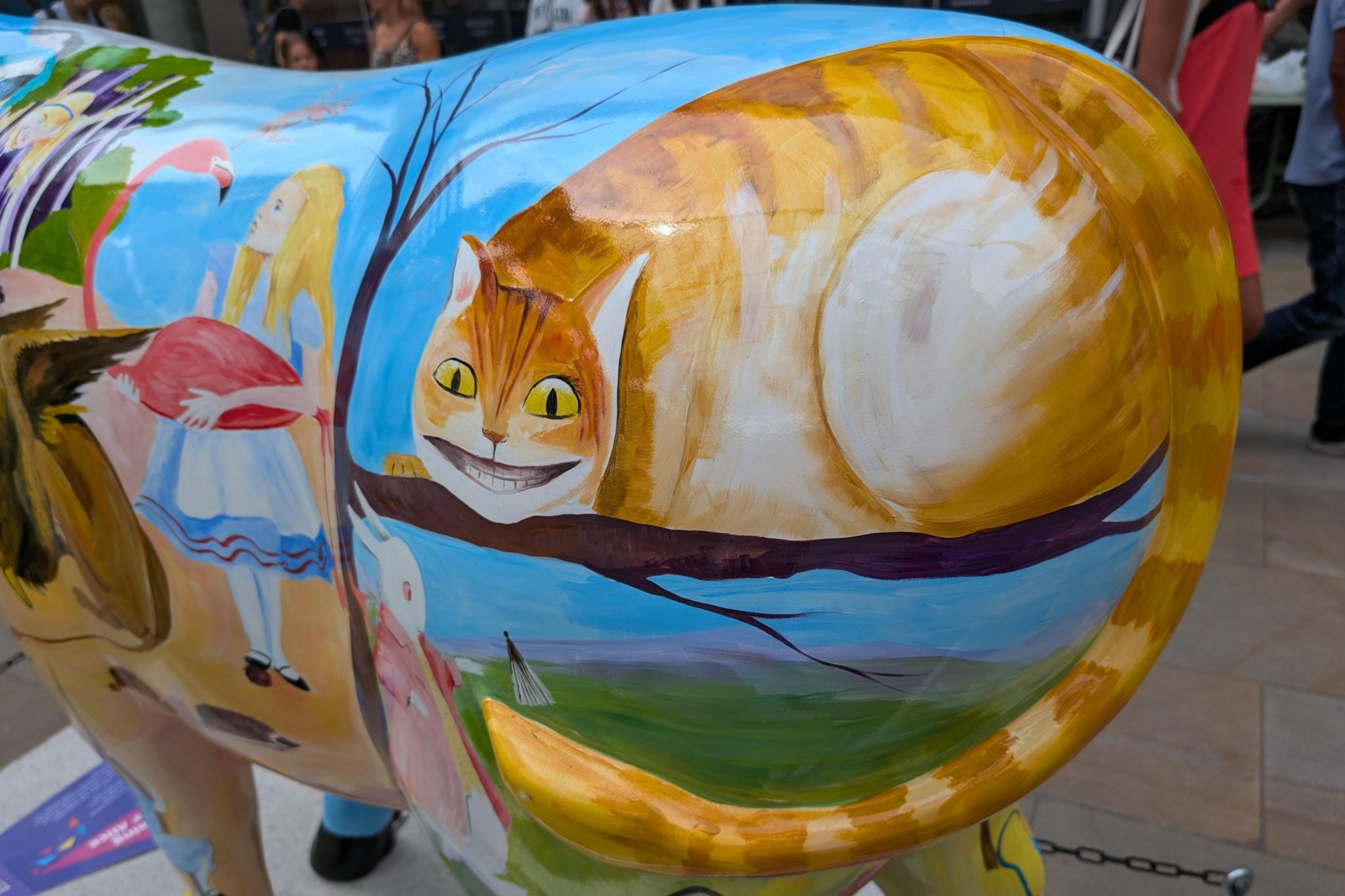 An illustration of Alice on Wonderland is painted onto the life size sculpture of an Ox as part of a charity fundraising art trail around Oxford. A grinning image of the Cheshire Cat, the white rabbit and Alice holding a flamingo are seen.