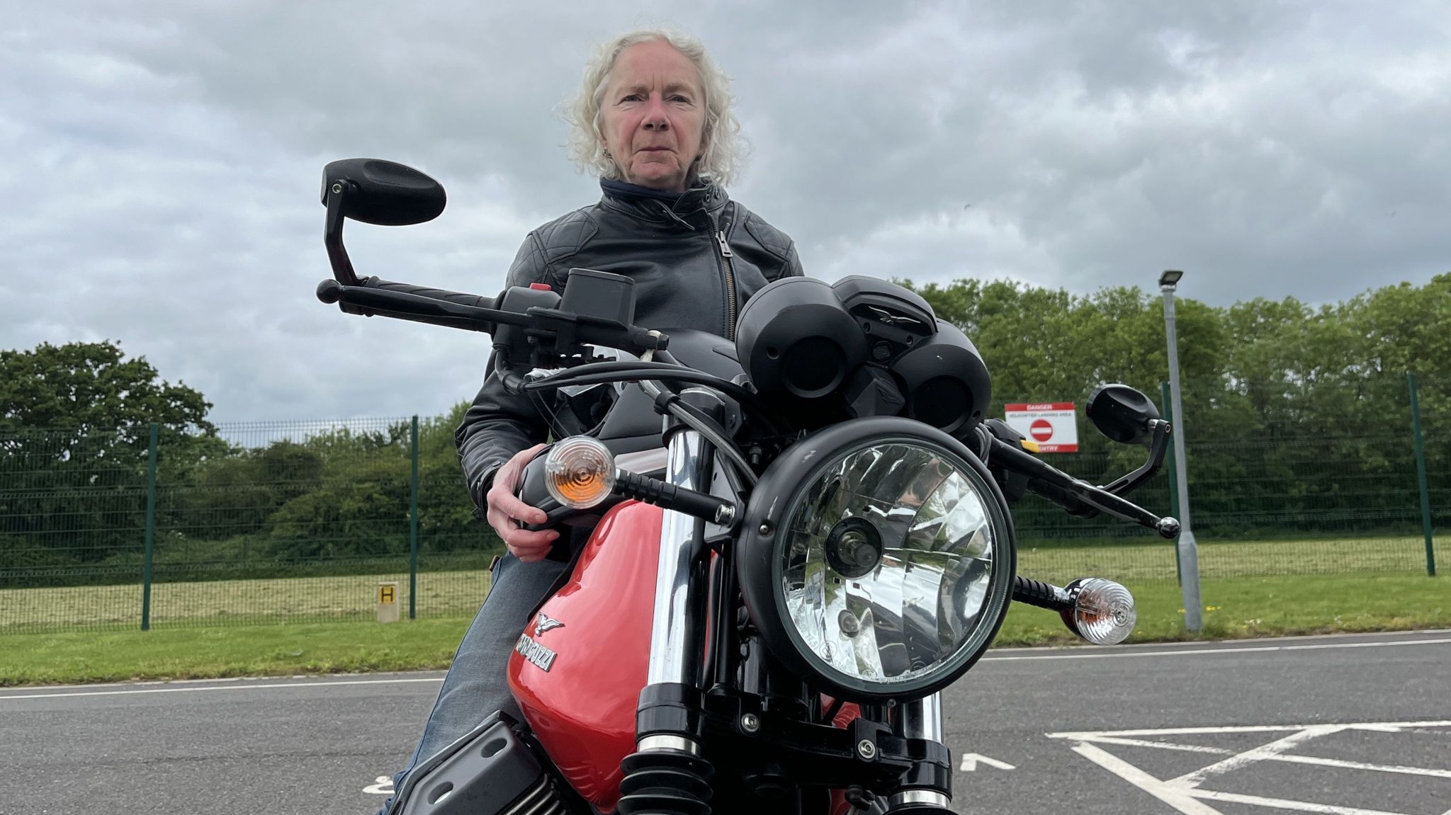 Julie Swain wearing her leather motorbike jacket and shoulder length blonde hair, sat on her motorbike parked outside the Wiltshire Air Ambulance airbase