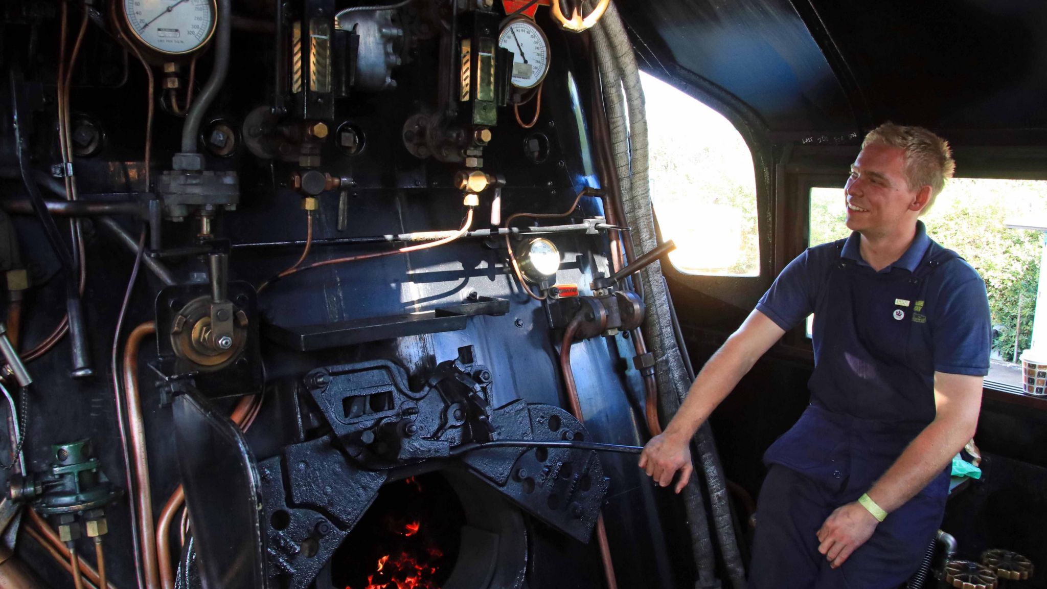 A man in one of the footplates of a steam locomotive adding coal to a furnice