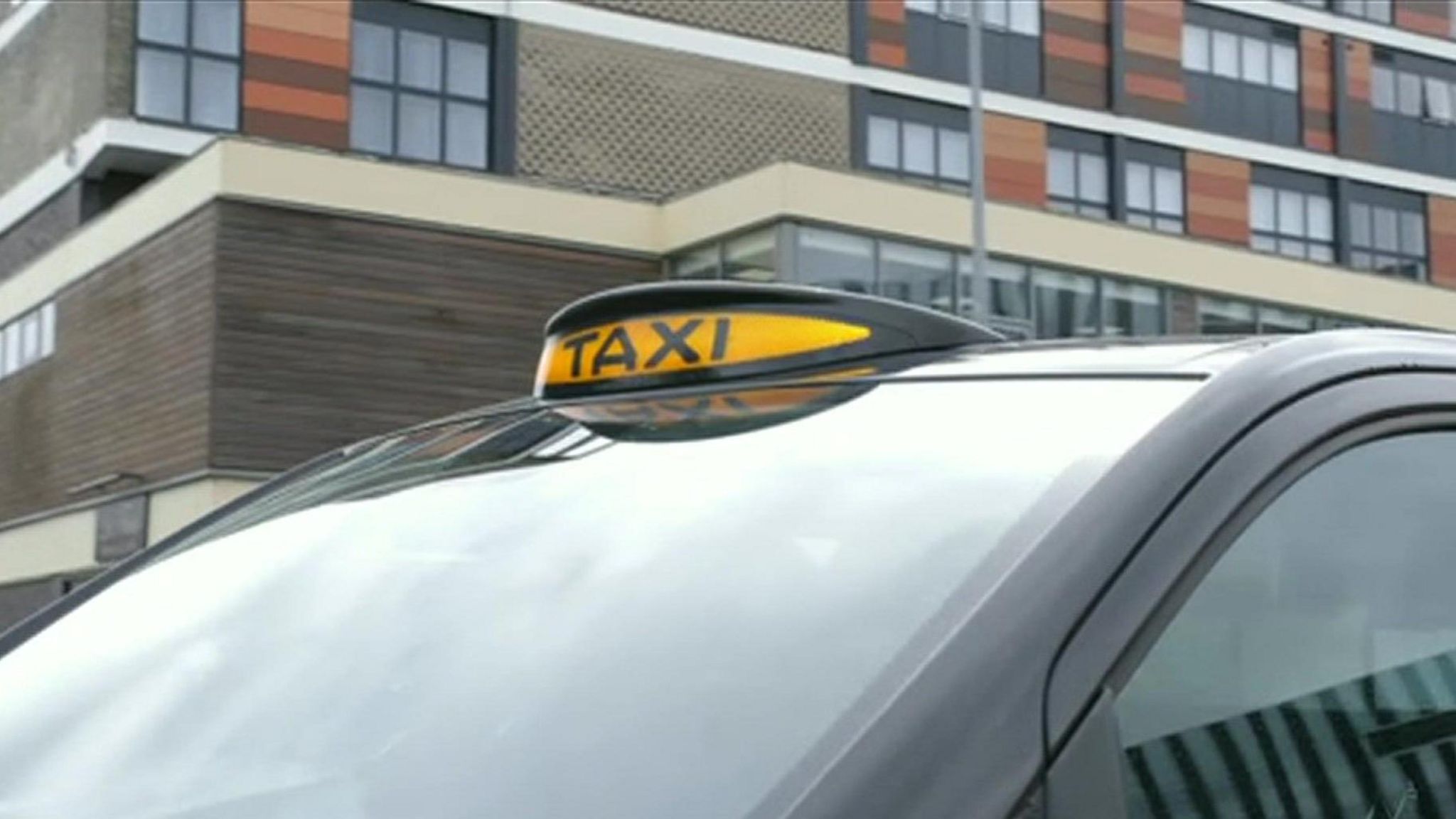 A close up of a black taxi with an orange 'taxi' sign on the top of the windscreen