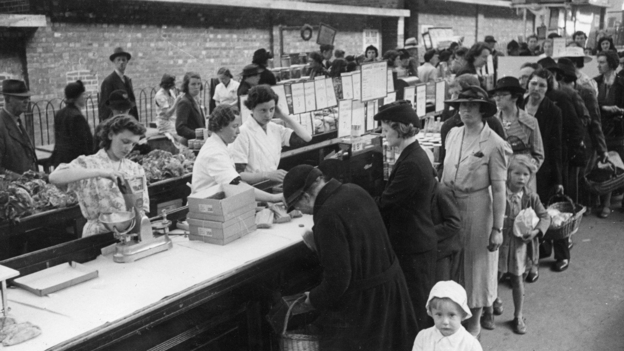 Shoppers queuing to buy food at a stall run by a department store at an open air market at Plymouth in the wake of German bombing during World War Two
