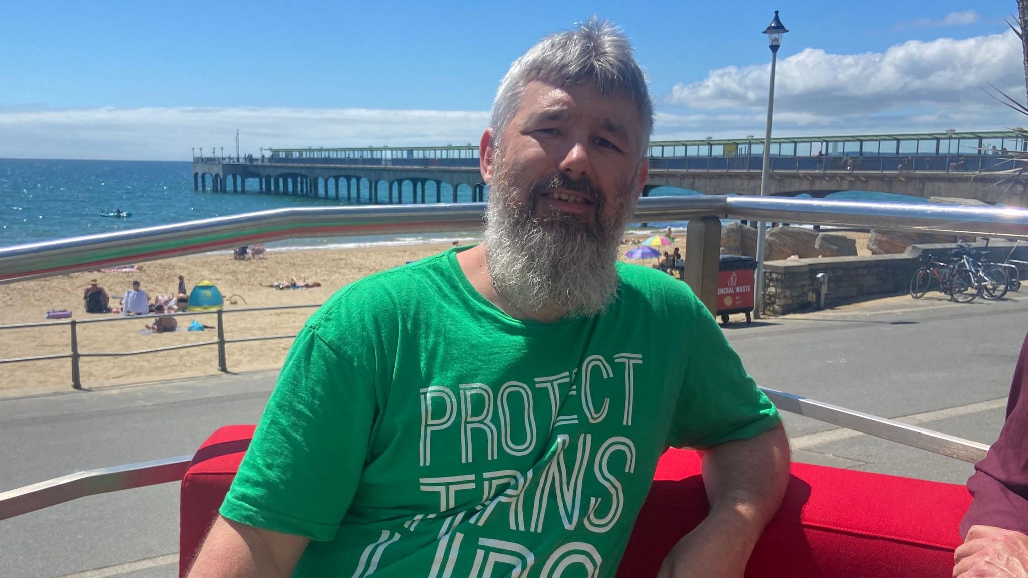 The Green Party's Joe Salmon is wearing a green t-shirt and has a grey beard. He sits on a red sofa.