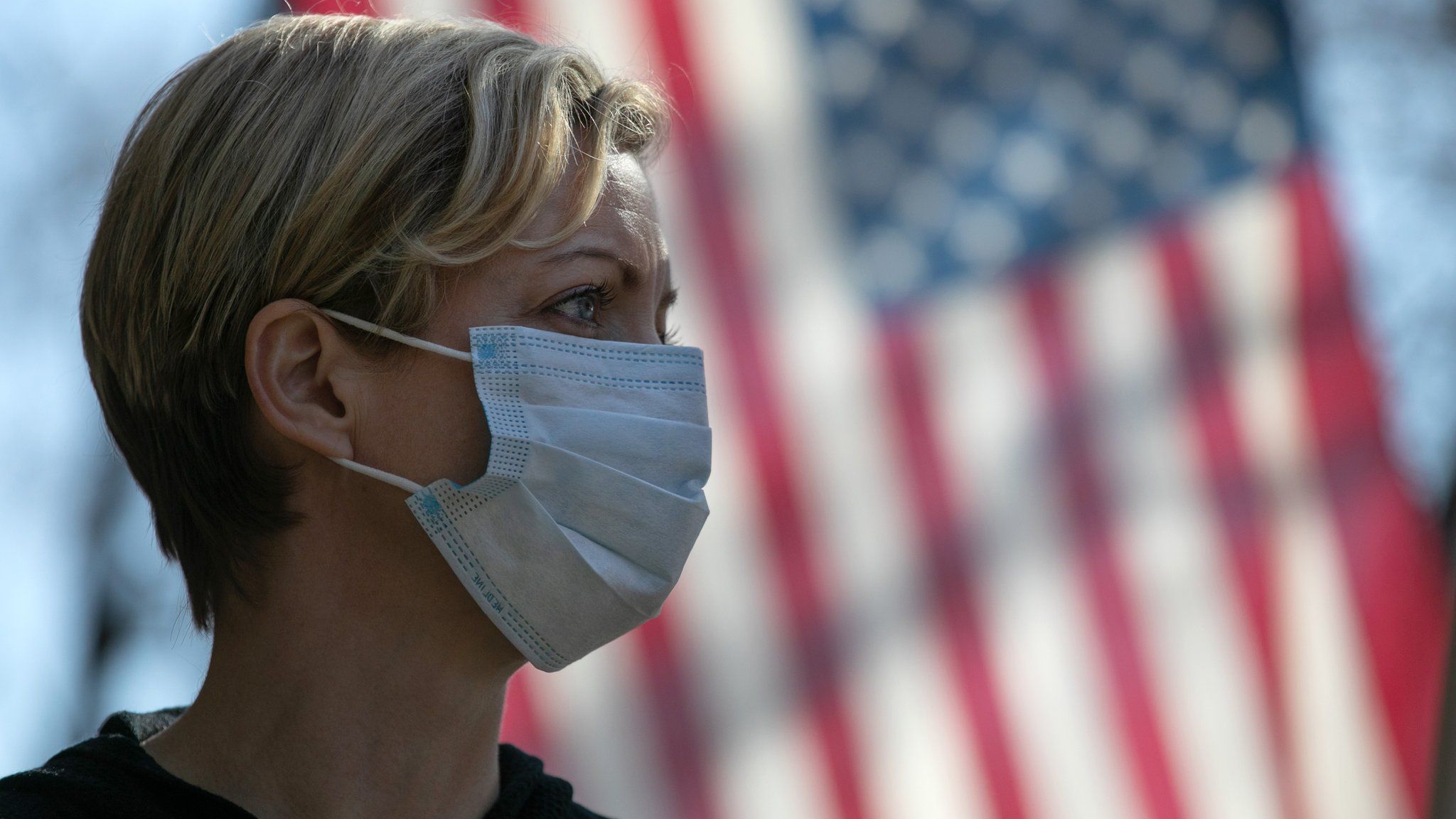 a woman in a mask in front of the American flag