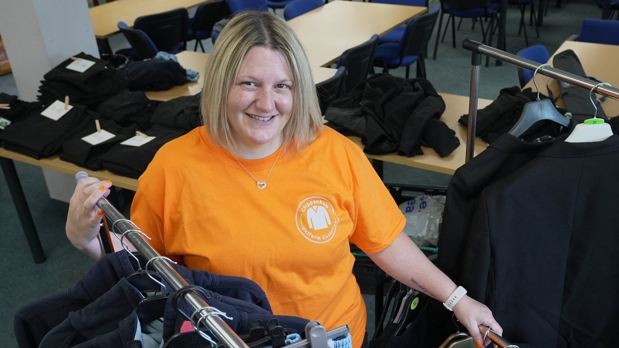 Woman in orange t-shirt looks up at camera surrounded by rails of school uniform.