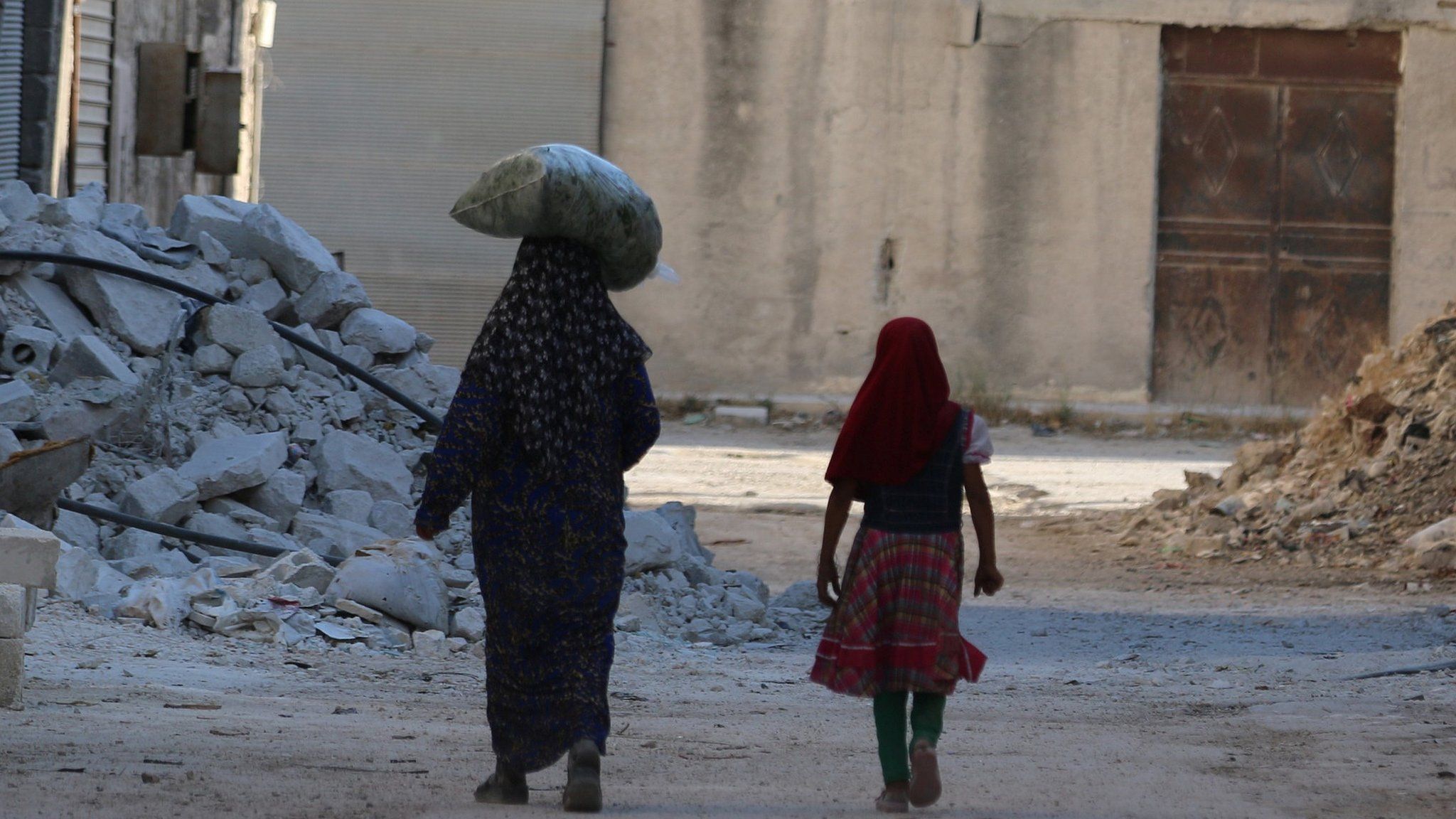 Civilians walk past damaged buildings