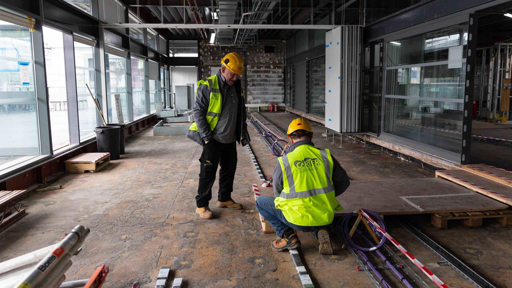 Workmen in high-viz jackets inside a building site with tools and fittings around them