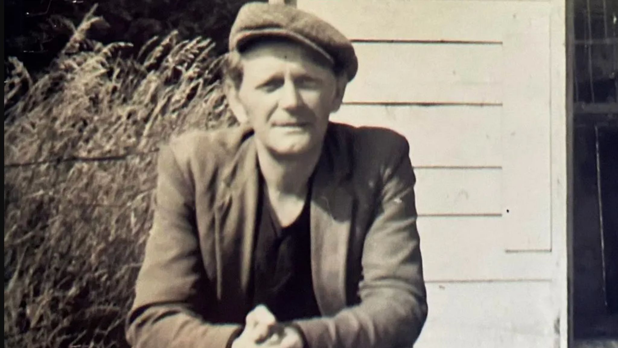 Black and white photo of 54-year-old Alfred Swinscoe wearing a flat cap and standing in front of his shed 