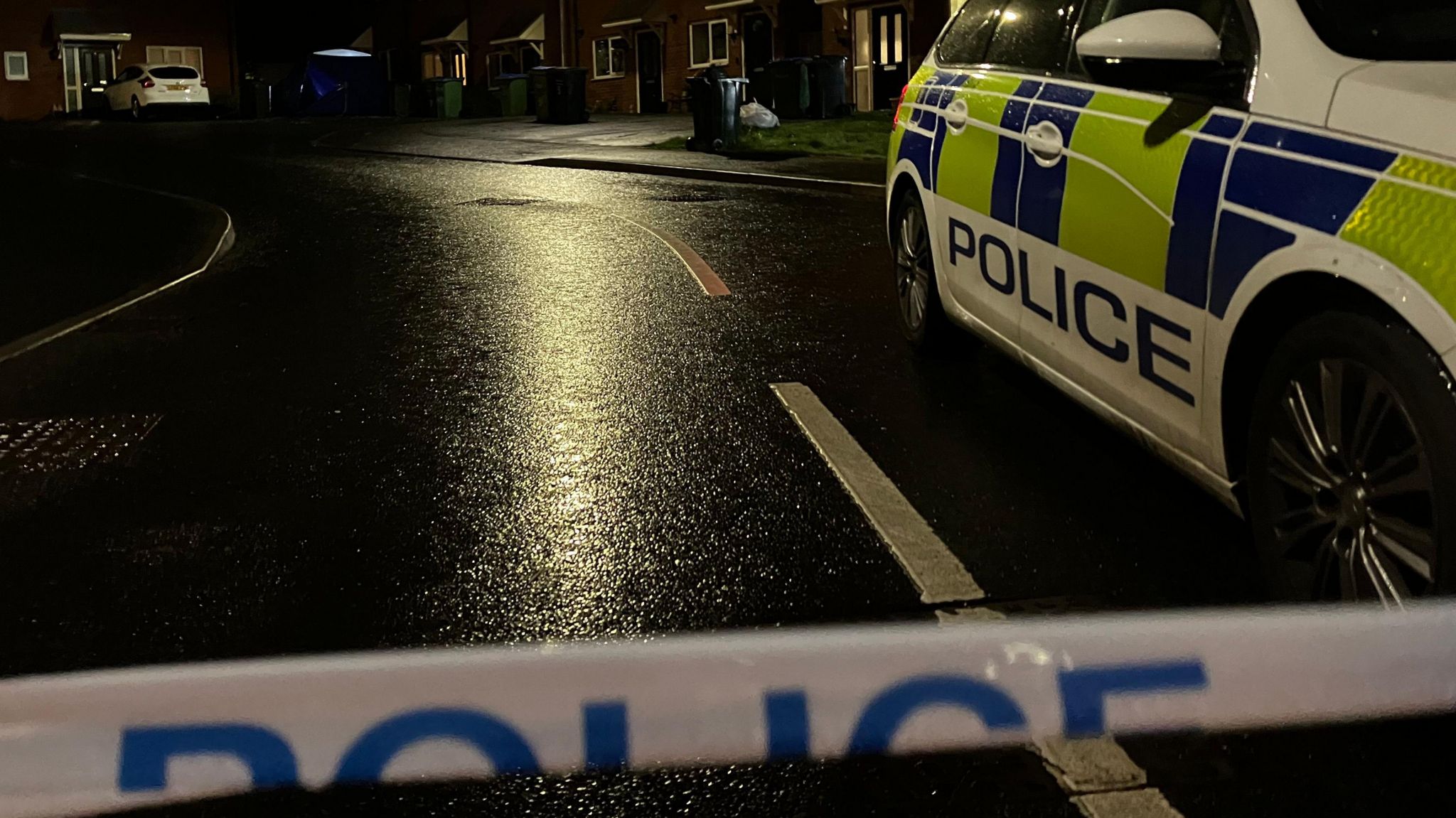 Police tape and a Police car on a wet road.