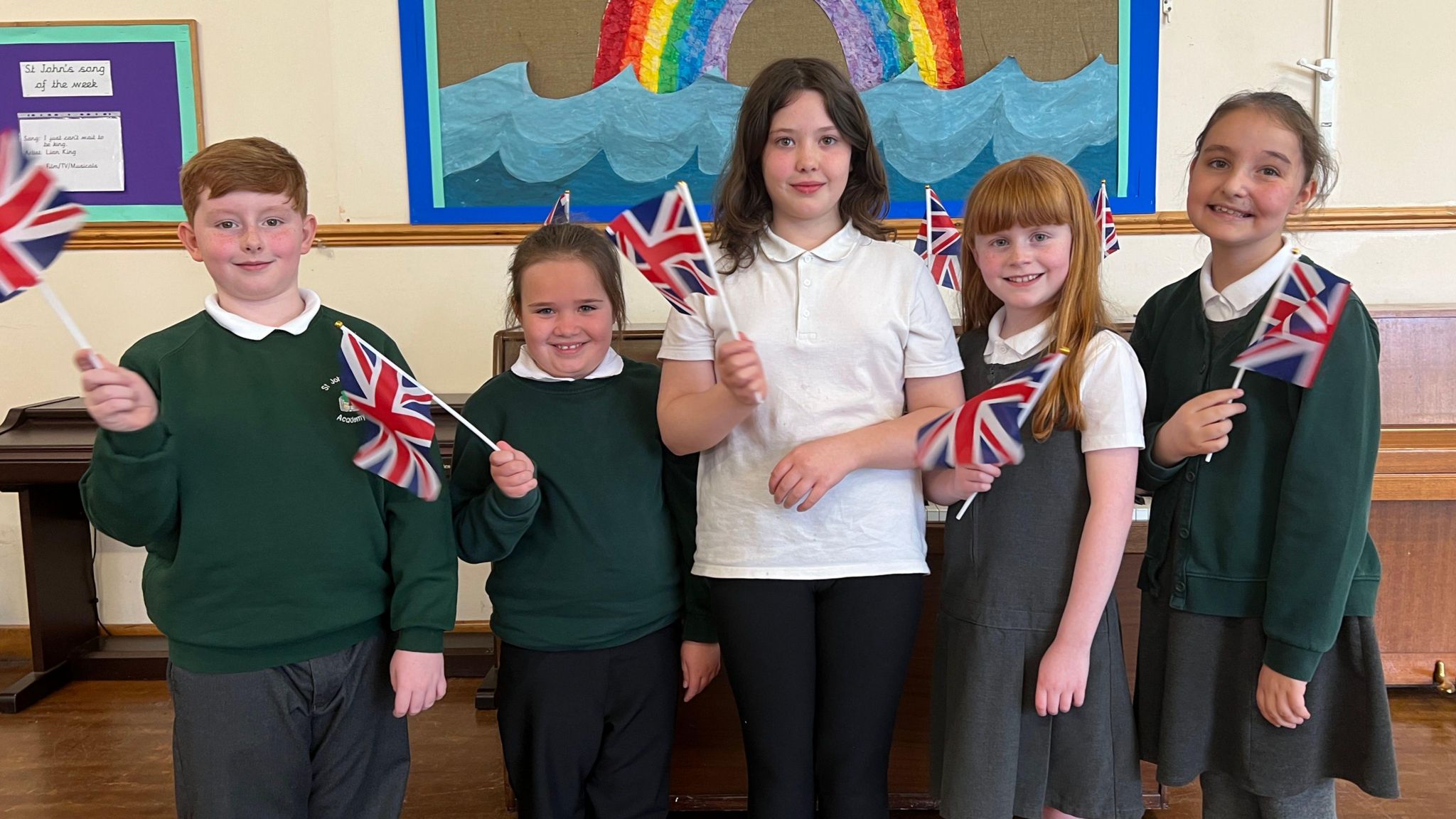 Five primary school pupils - one boy and four girls - waving Union flags in a line